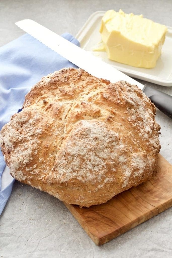 Soda bread loaf on a board with bread knife and butter.