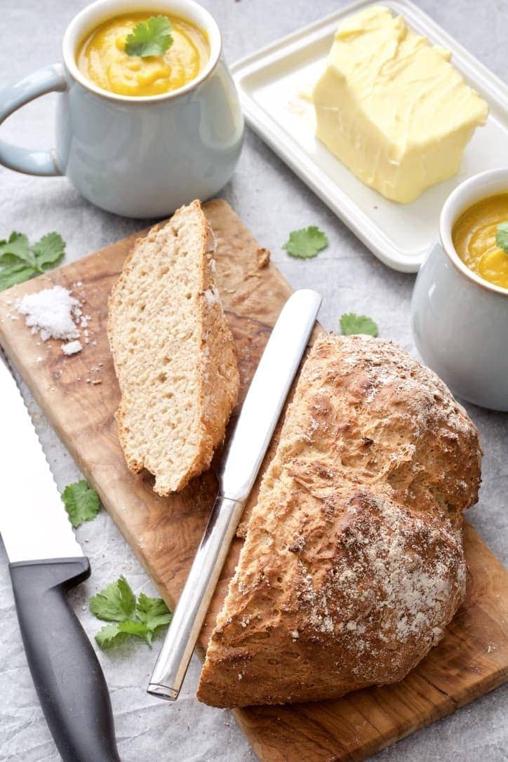 Bread loaf on cutting board with large slice cut off, soup & butter.