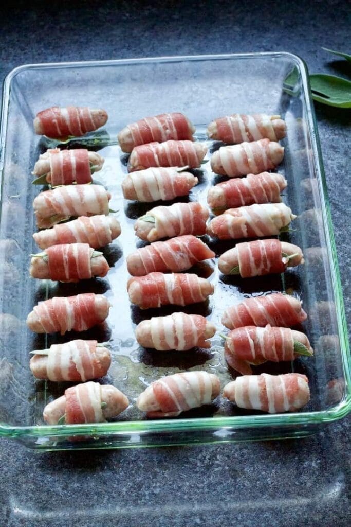 Raw cocktail sausages wrapped in bacon in a dish.