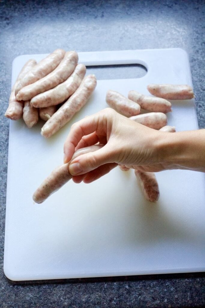 Hand squeezing chipolata in half.