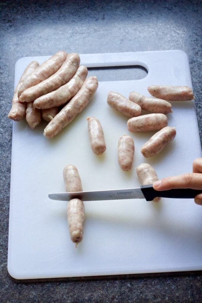 Knife cutting chipolata in half.