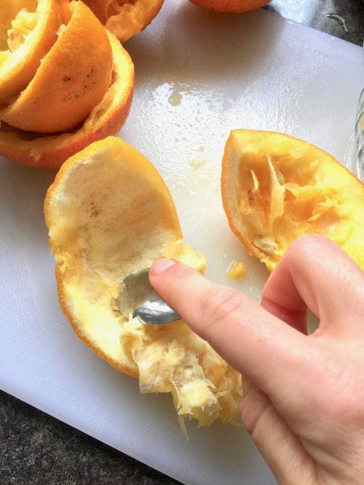 Scraping white pith from the orange rind with a spoon.