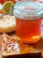 Jar of orange marmalade with piece of toast next to it.