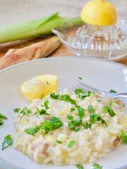 Portion of risotto in a bowl with lemon wedge.