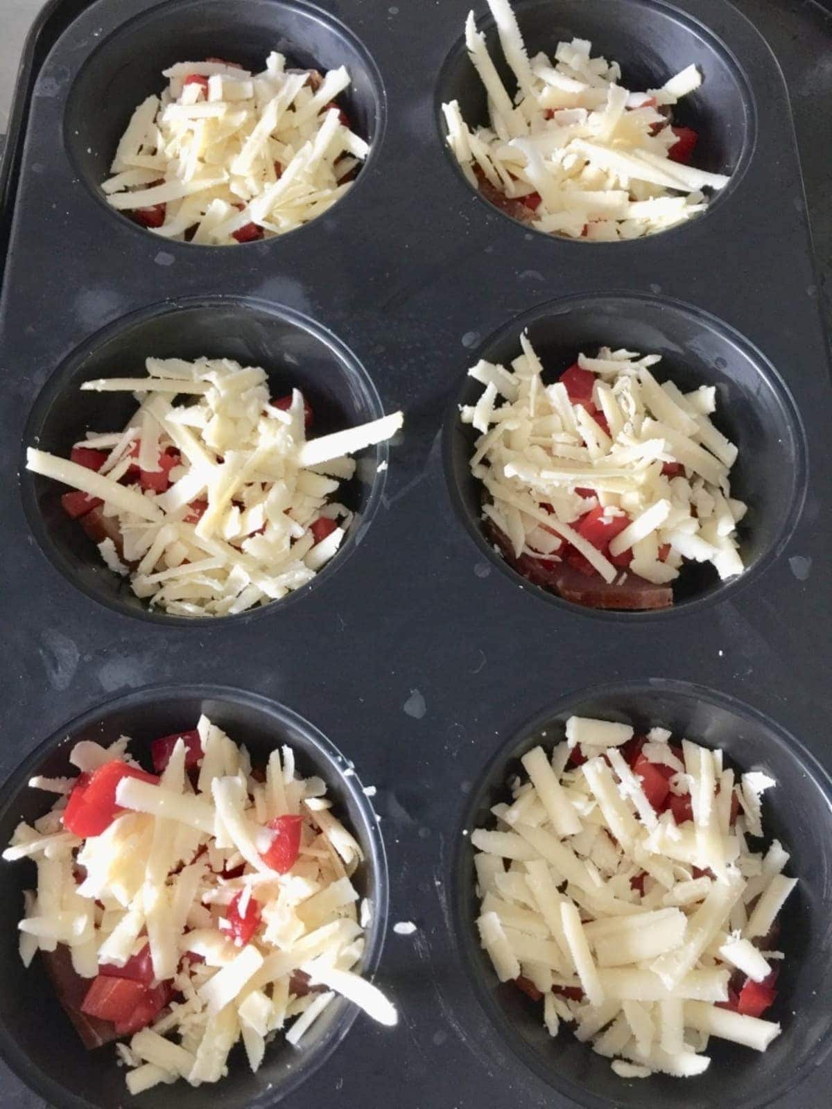 Pepper pieces & grated cheese in a muffin tin.