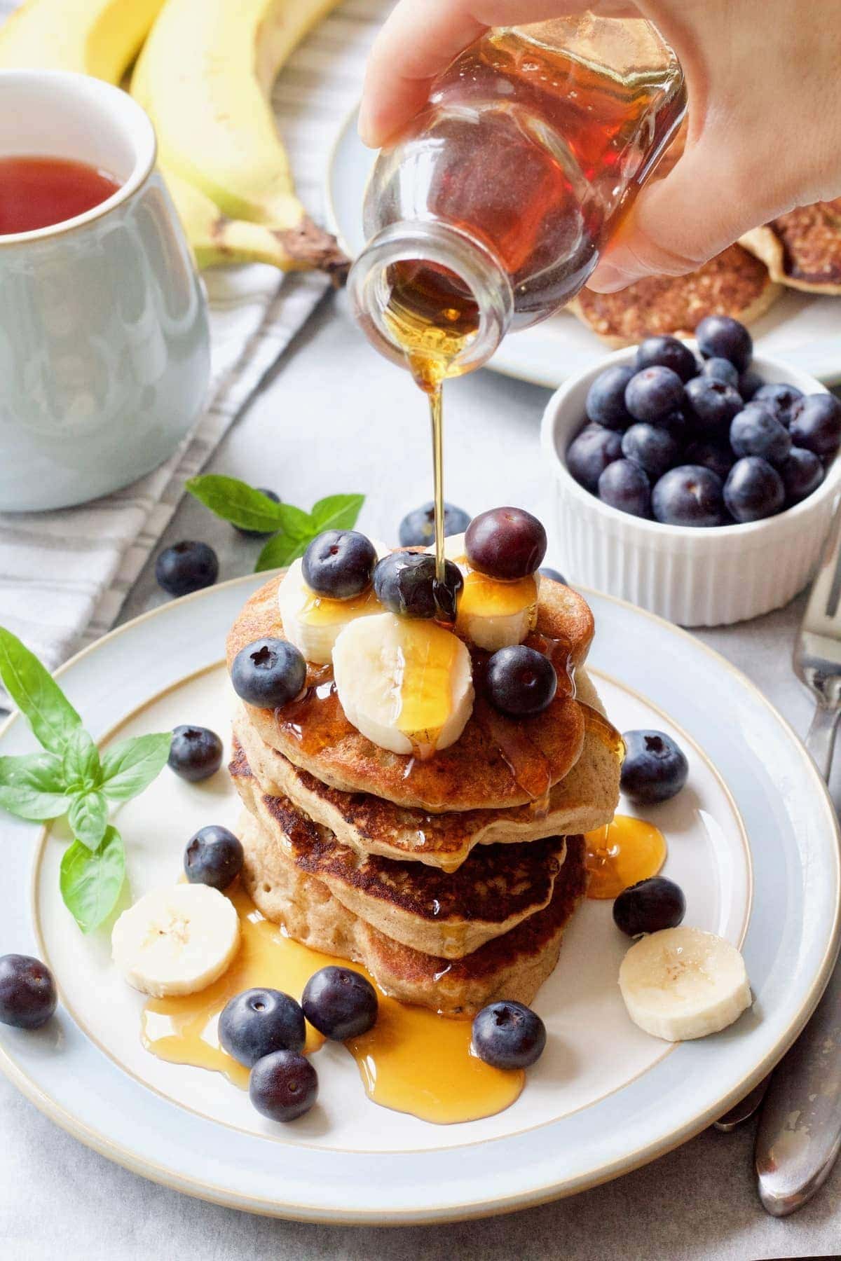 Maple syrup being poured over stack of pancakes.