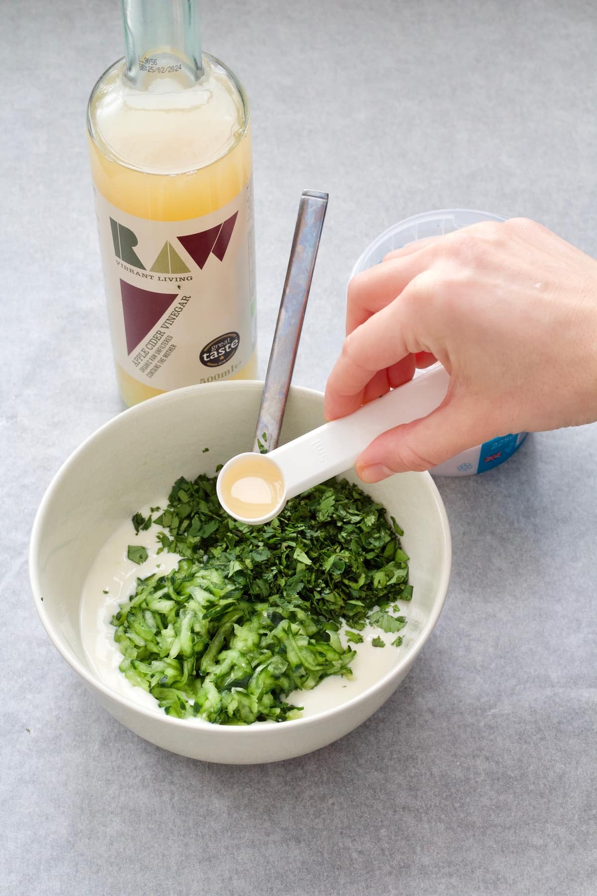 Adding vinegar to a bowl of yogurt sauce.