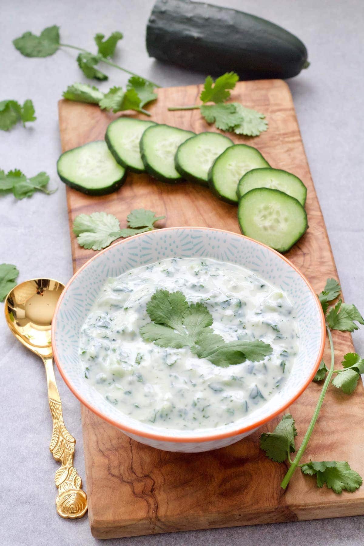 Cucumber raita in a bowl on a bamboo board.