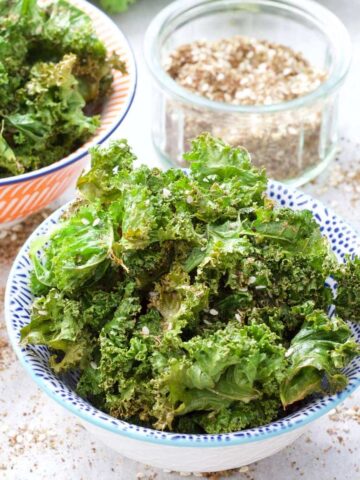Kale crisps in a bowl with bowl of seasoning behind.