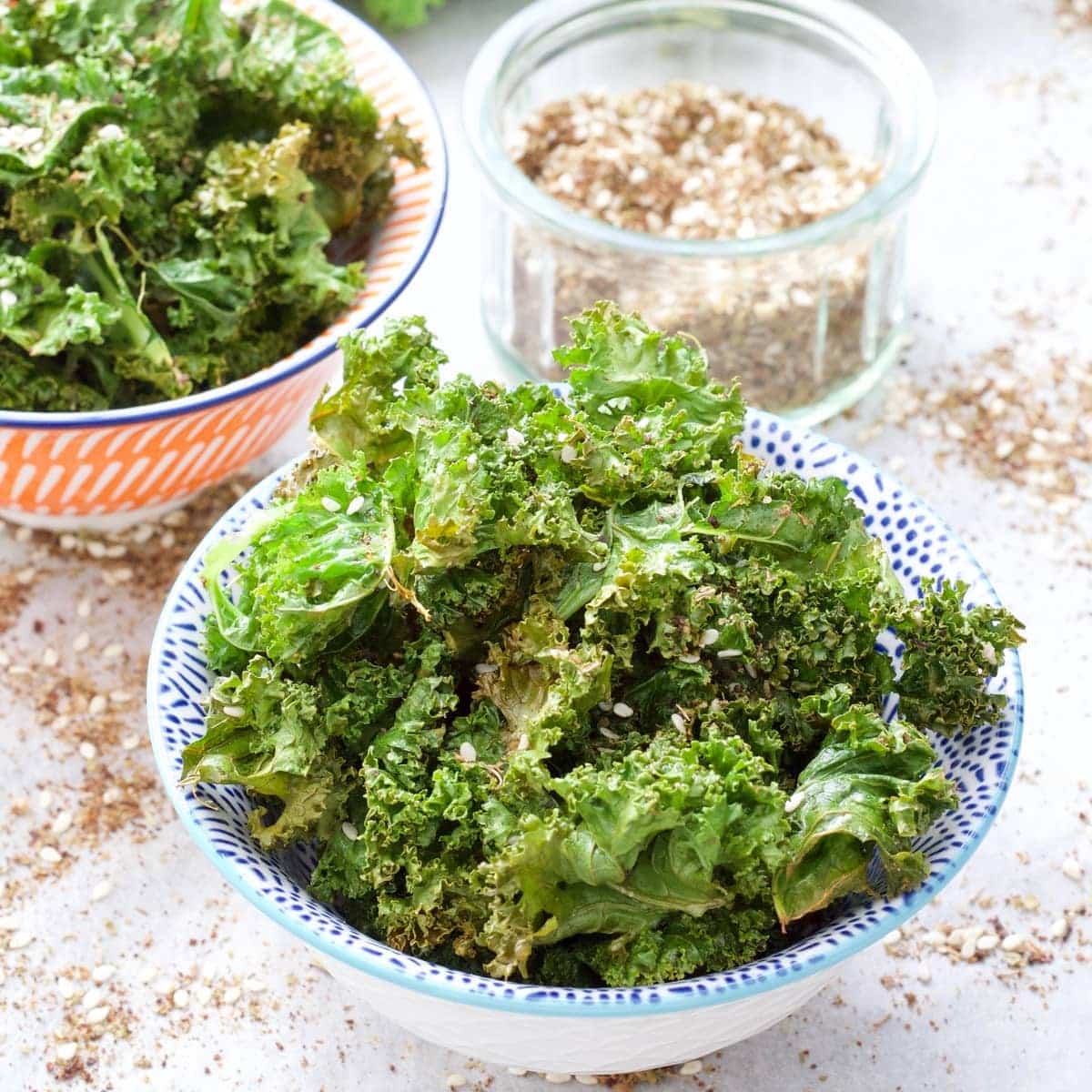 Kale crisps in a bowl with bowl of seasoning behind.