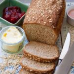 Bread with couple slices cut off, butter, jam & knives.