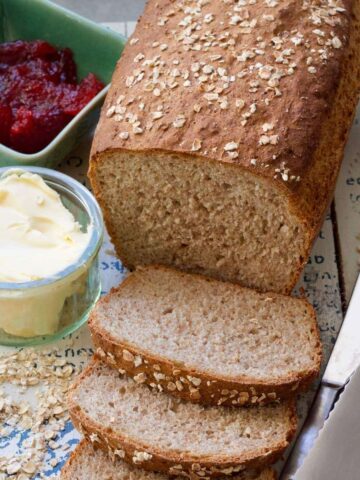 Bread with couple slices cut off, butter, jam & knives.