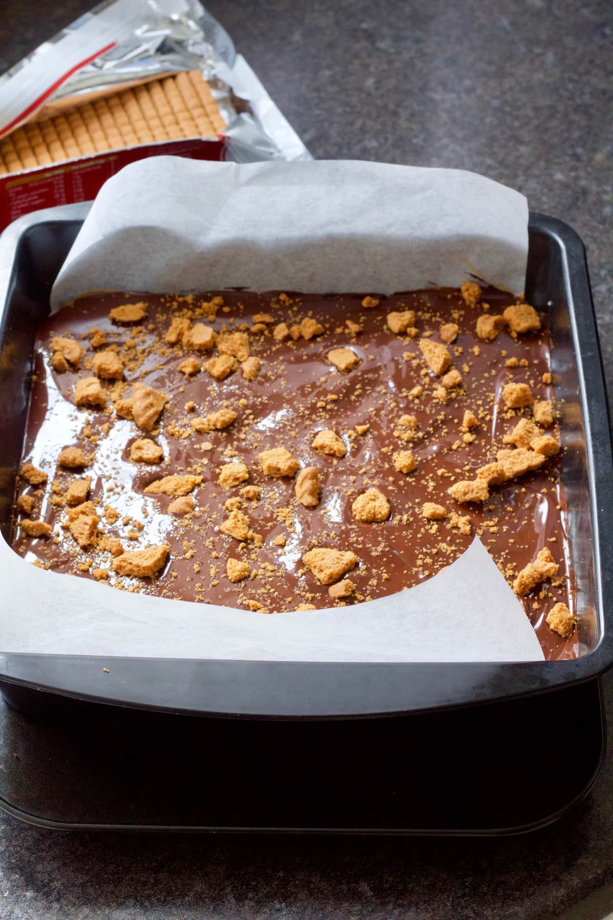 Tin with millionaire's shortbread showing top layer of chocolate and crushed biscuits.