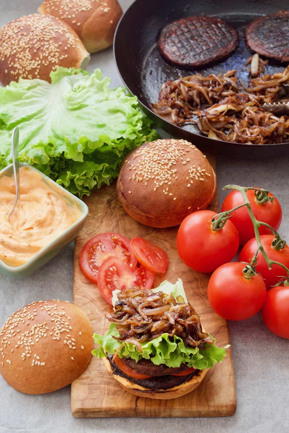 Portobello mushroom burger assembly with buns, tomatoes & lettuce.