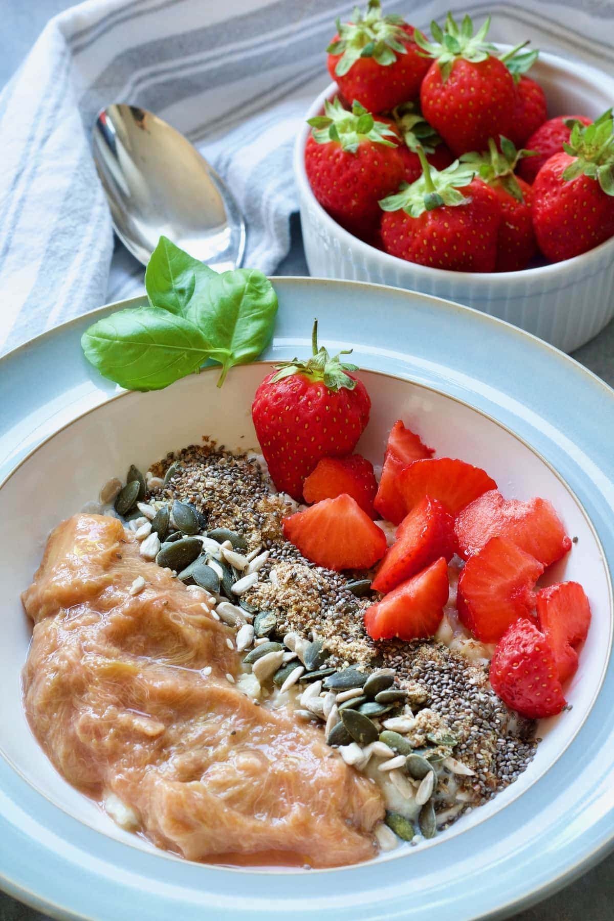 Bowl of porridge topped with stewed rhubarb, strawberries and seeds.