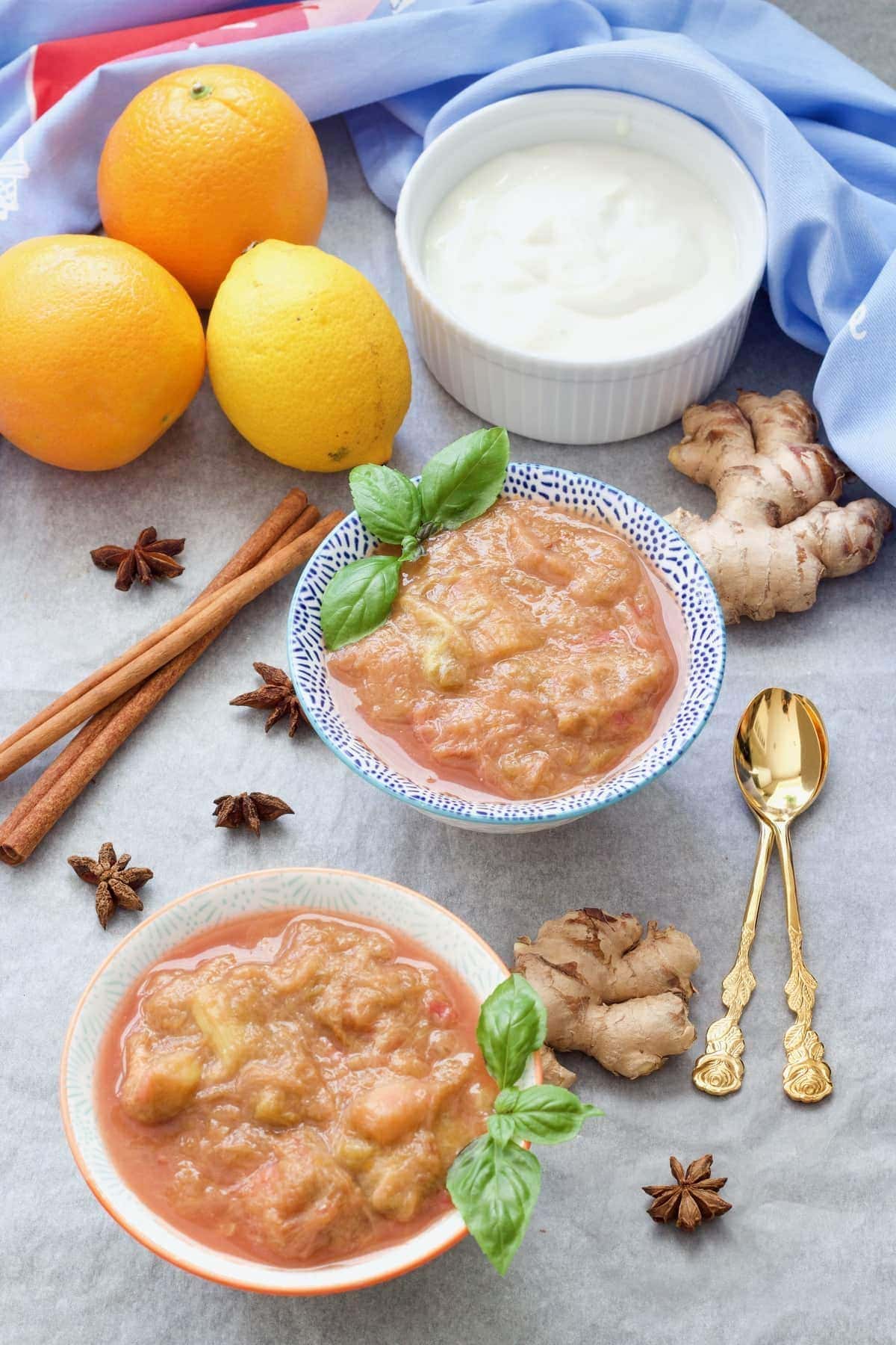 Stewed rhubarb in bowls with fruit, yogurt & ginger roots around it.