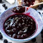 Spoonful of blackberry jam over a bowl with jam, close up.