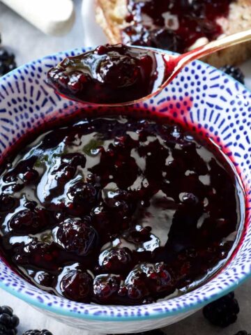 Spoonful of blackberry jam over a bowl with jam, close up.