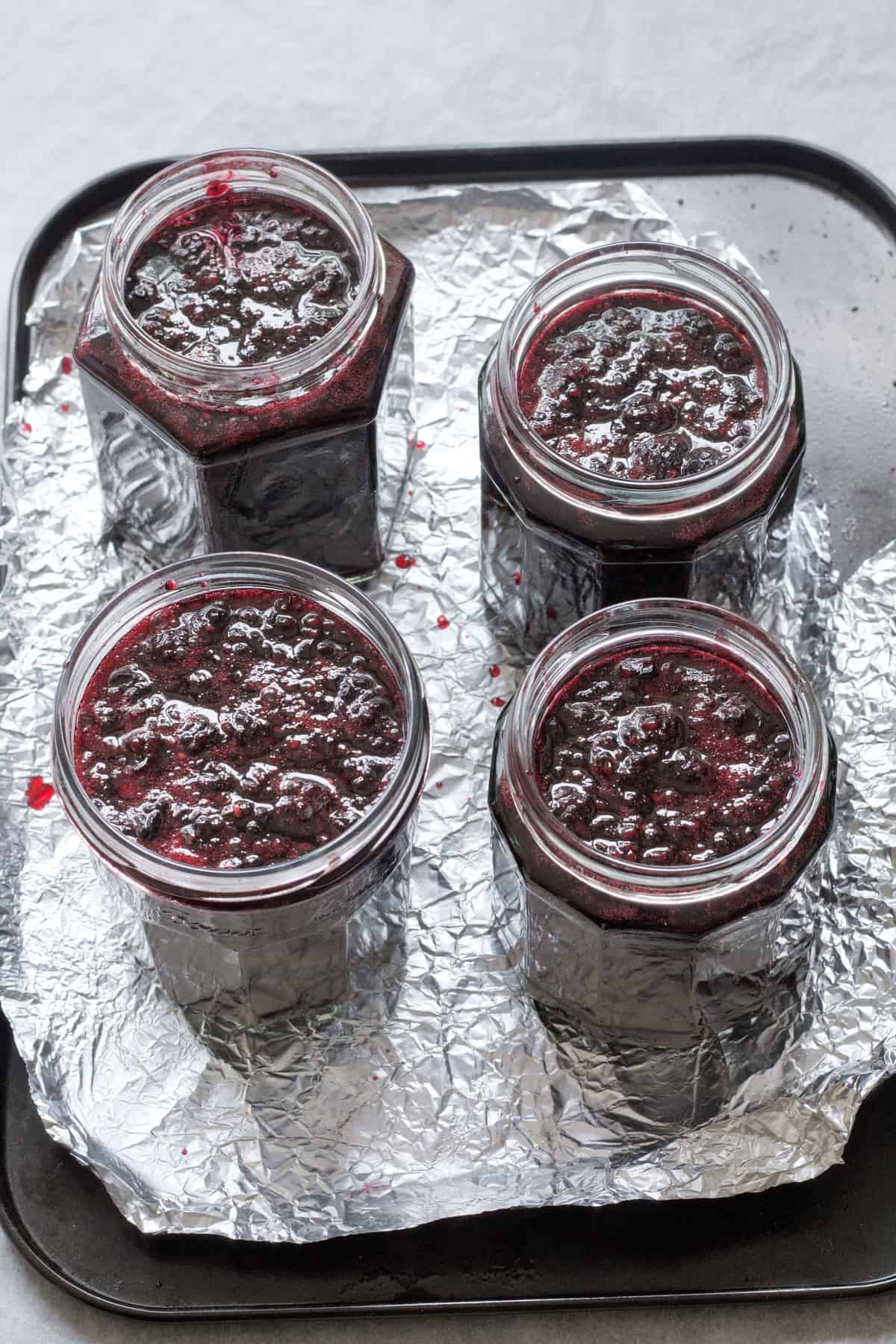 Four jars filled with blackberry jam on a tray.