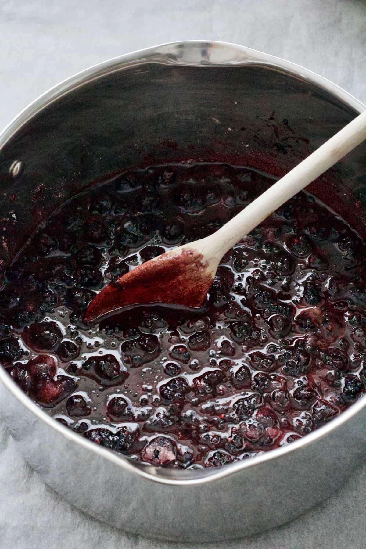 Large pan with jam mixture and wooden spoon in it.