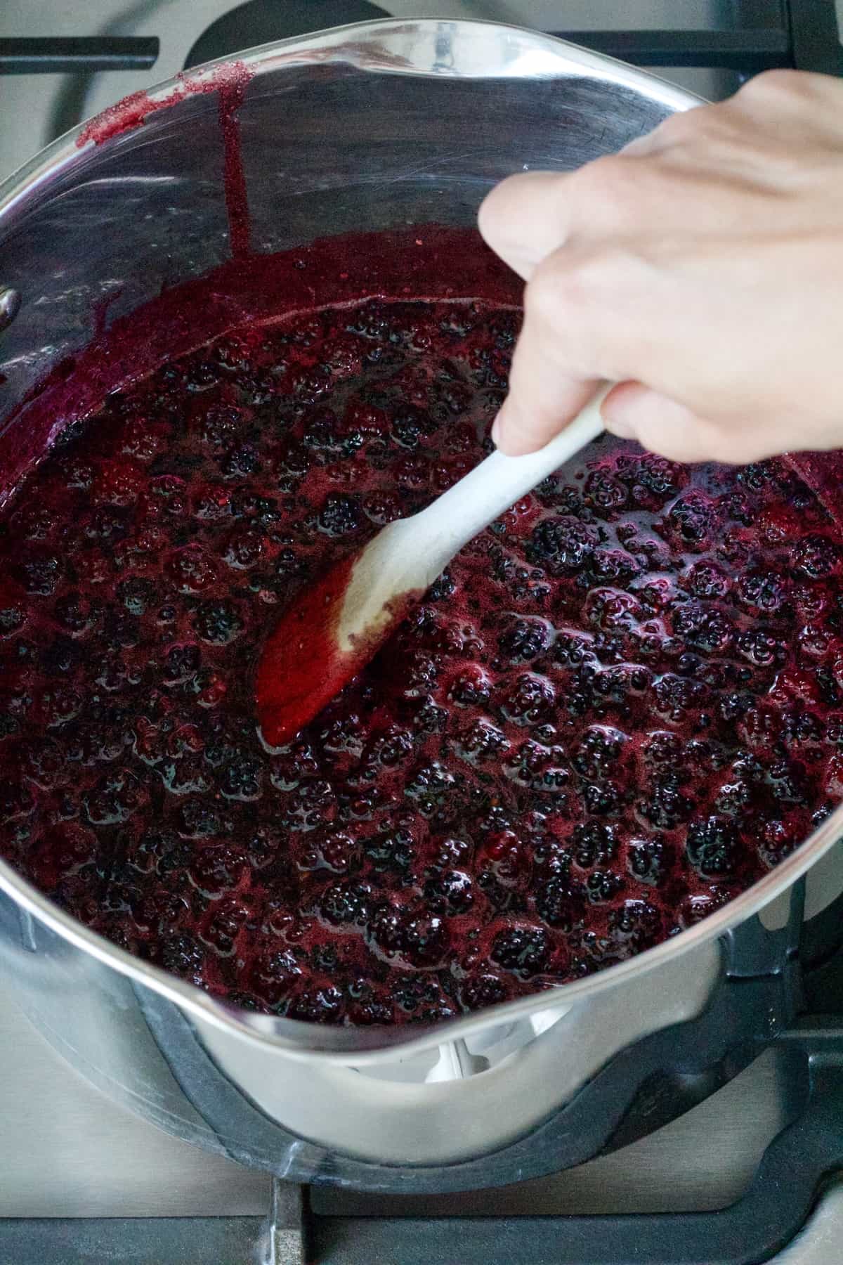 Hand stirring jam mixture in a pan with wooden spoon.