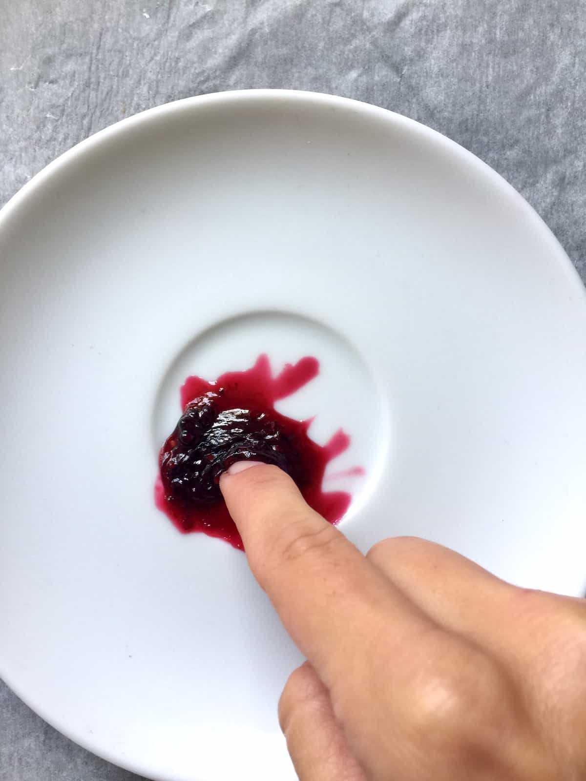 Finger pushing jam on a plate.