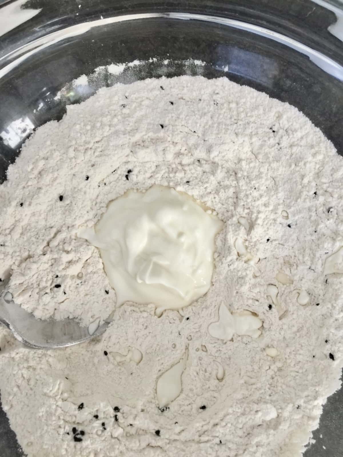 Flour & black nigella seeds in a bowl with dollop of yogurt.