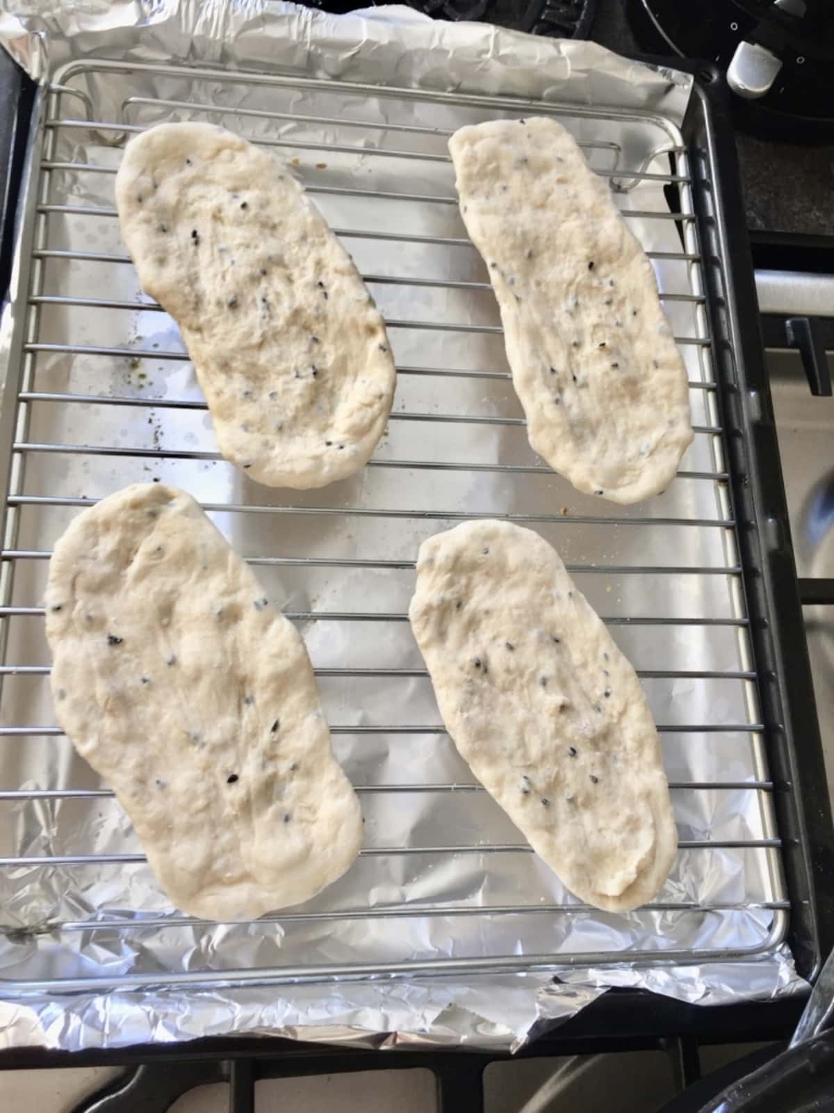 4 uncooked naan breads on a grill rack.