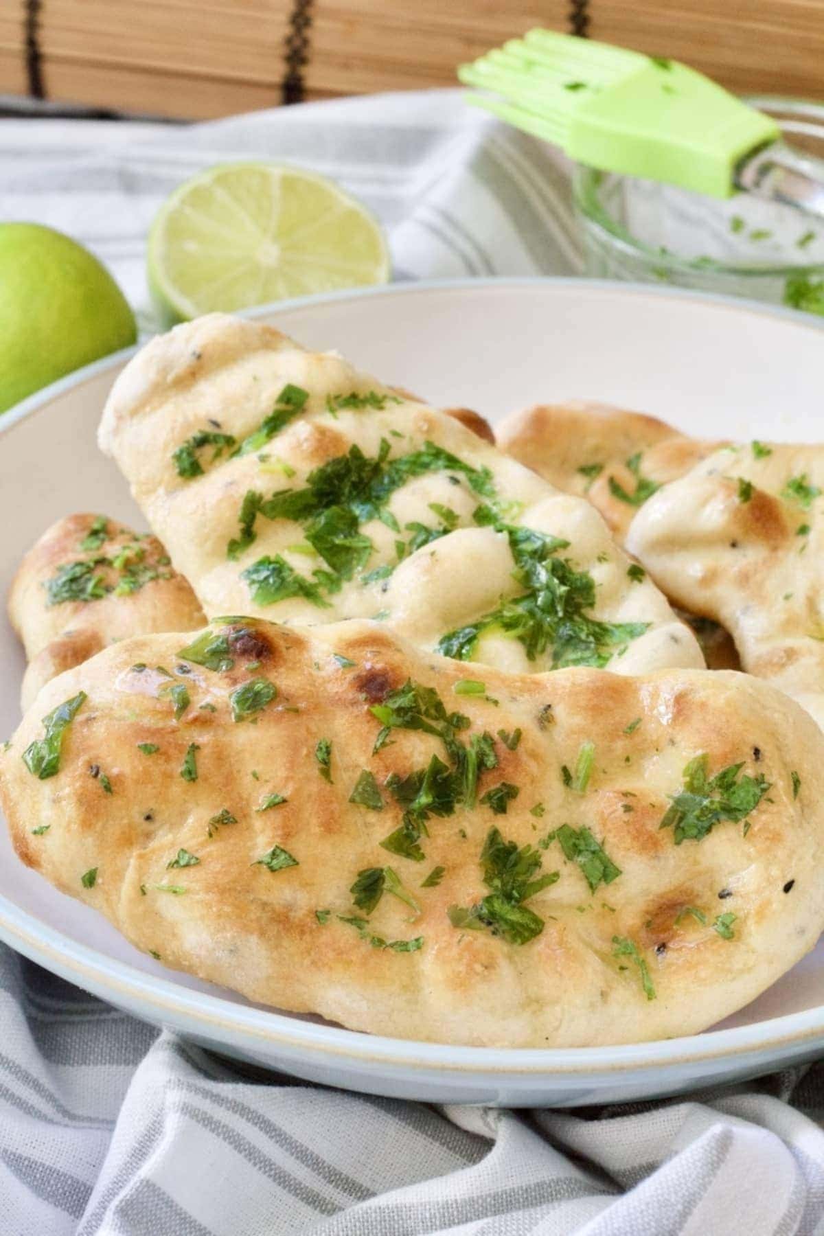 Cooked naan bread in a bowl brushed with herb butter.