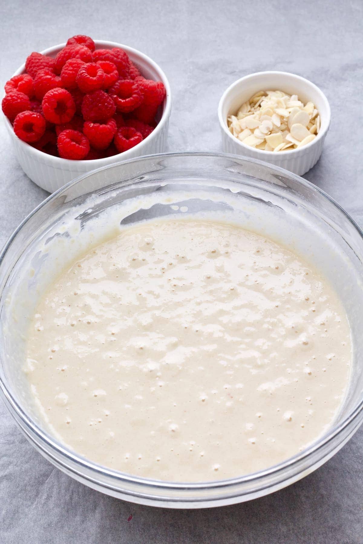 Cake batter in a bowl, fresh raspberries & flaked almonds.