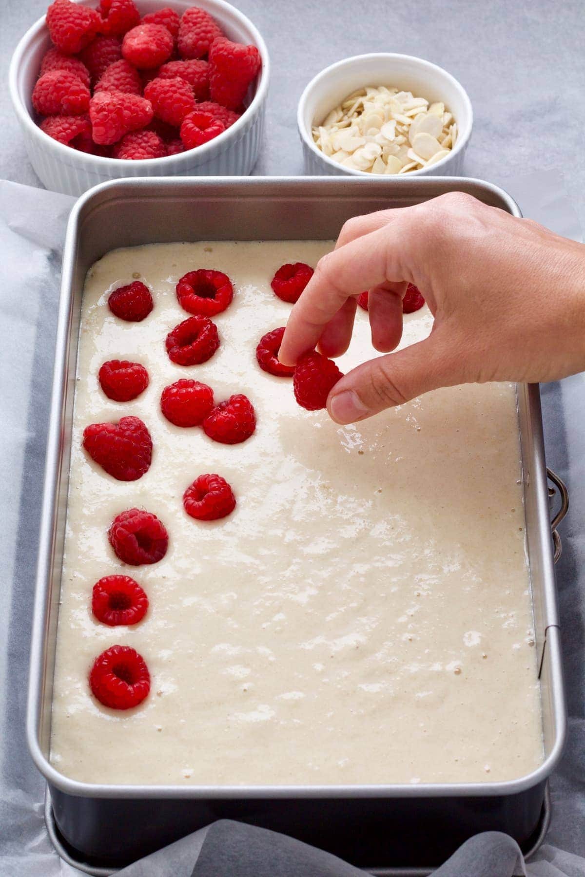 Hand putting raspberries on top of the cake batter.