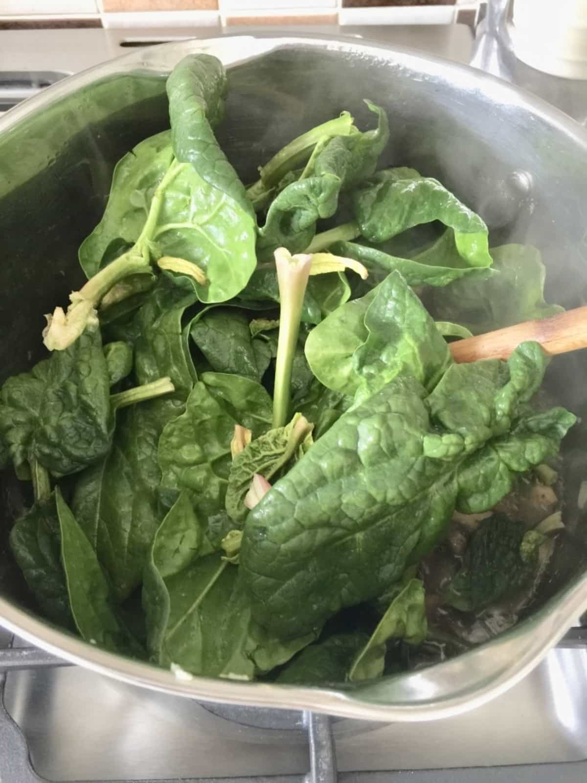 Fresh spinach leaves added to a large pot.