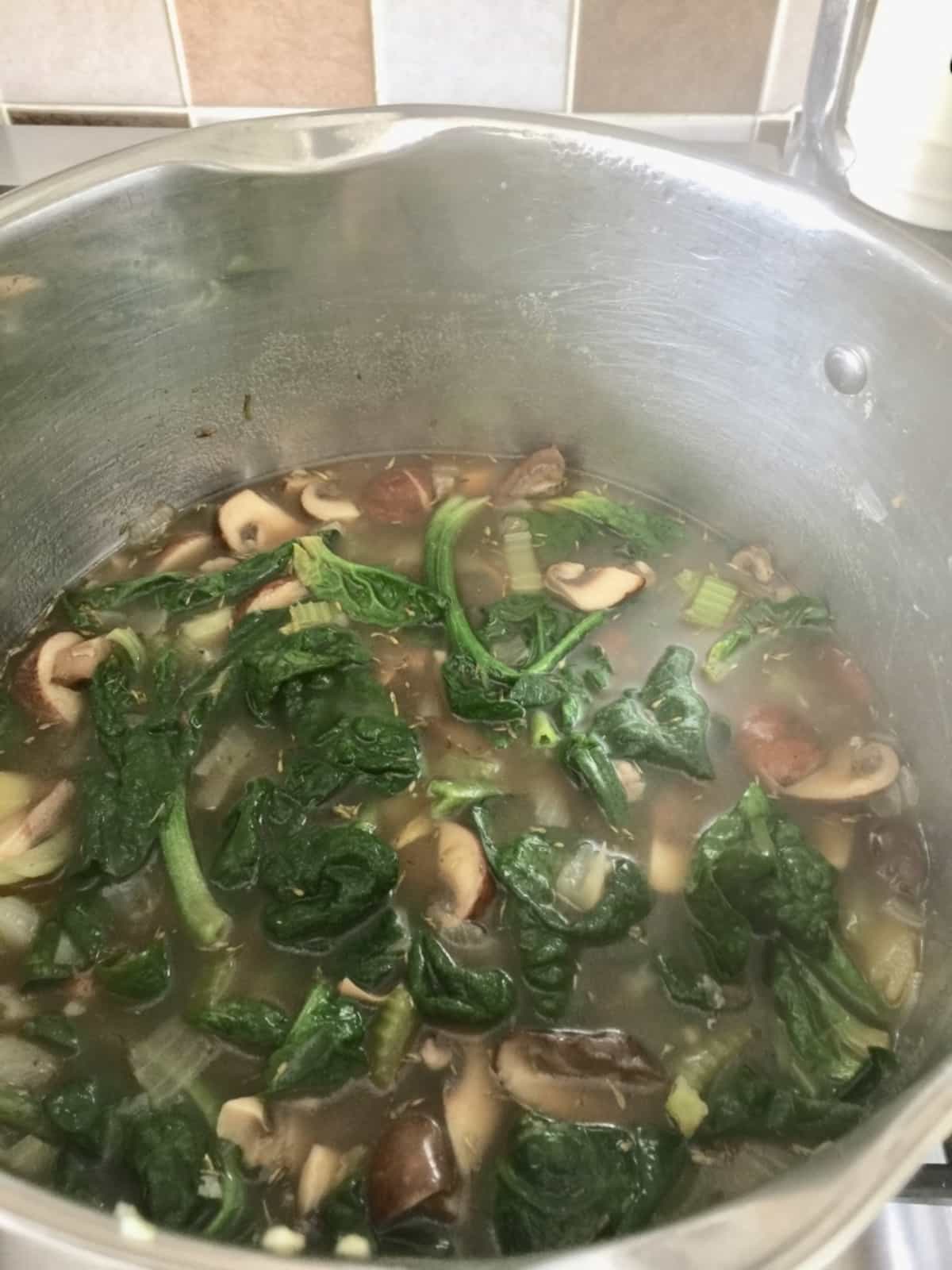 Large pot full of spinach and mushrooms in stock.