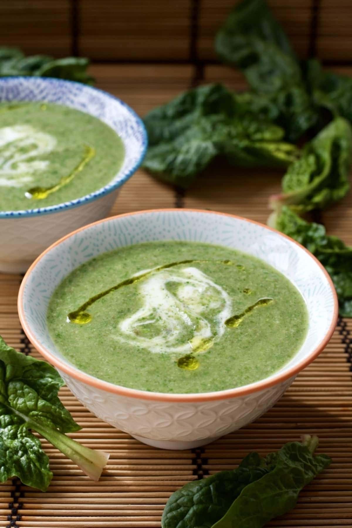 Small bowl of green soup with spinach leaves around.