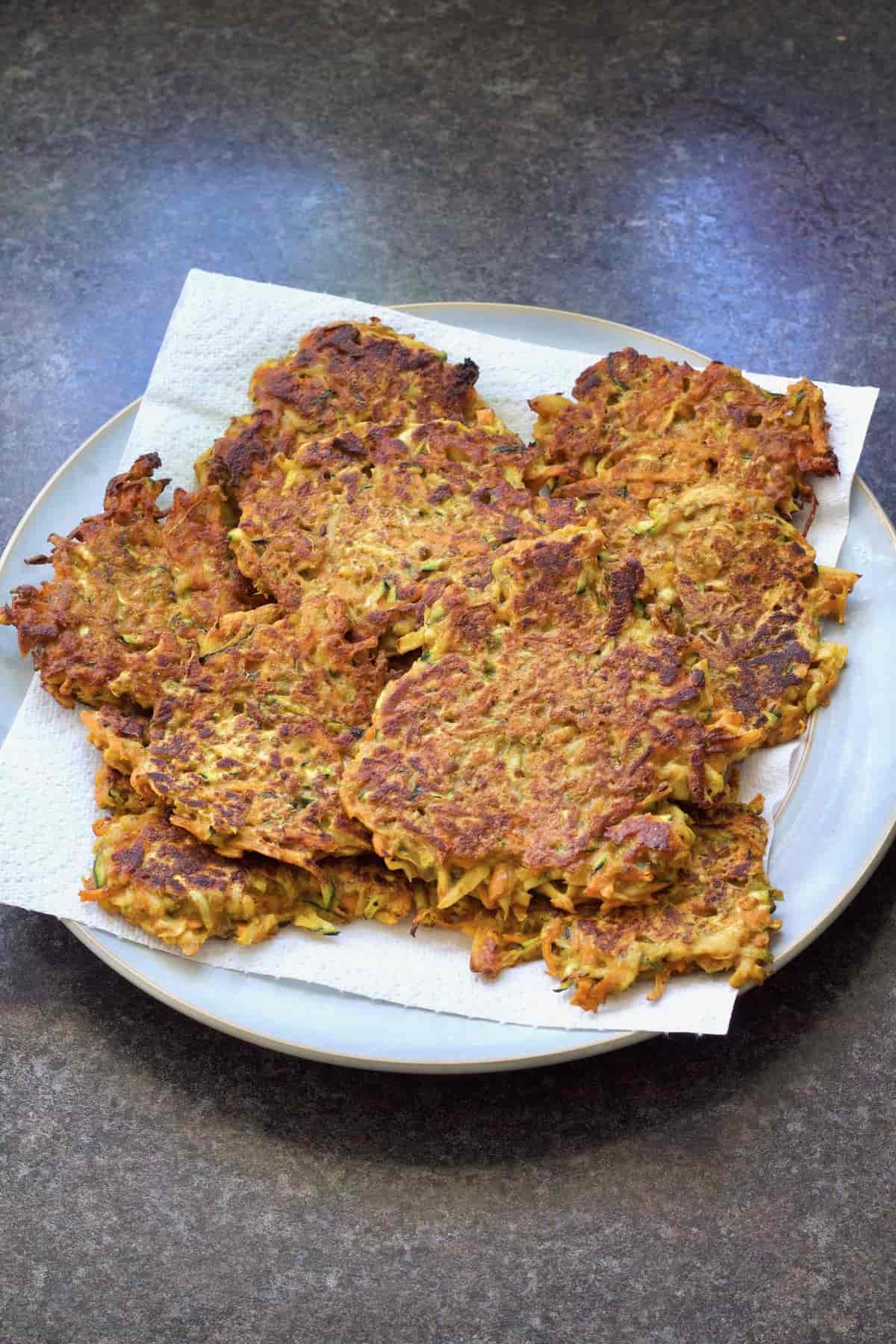 Fritters piled up on a plate on top of paper towel.