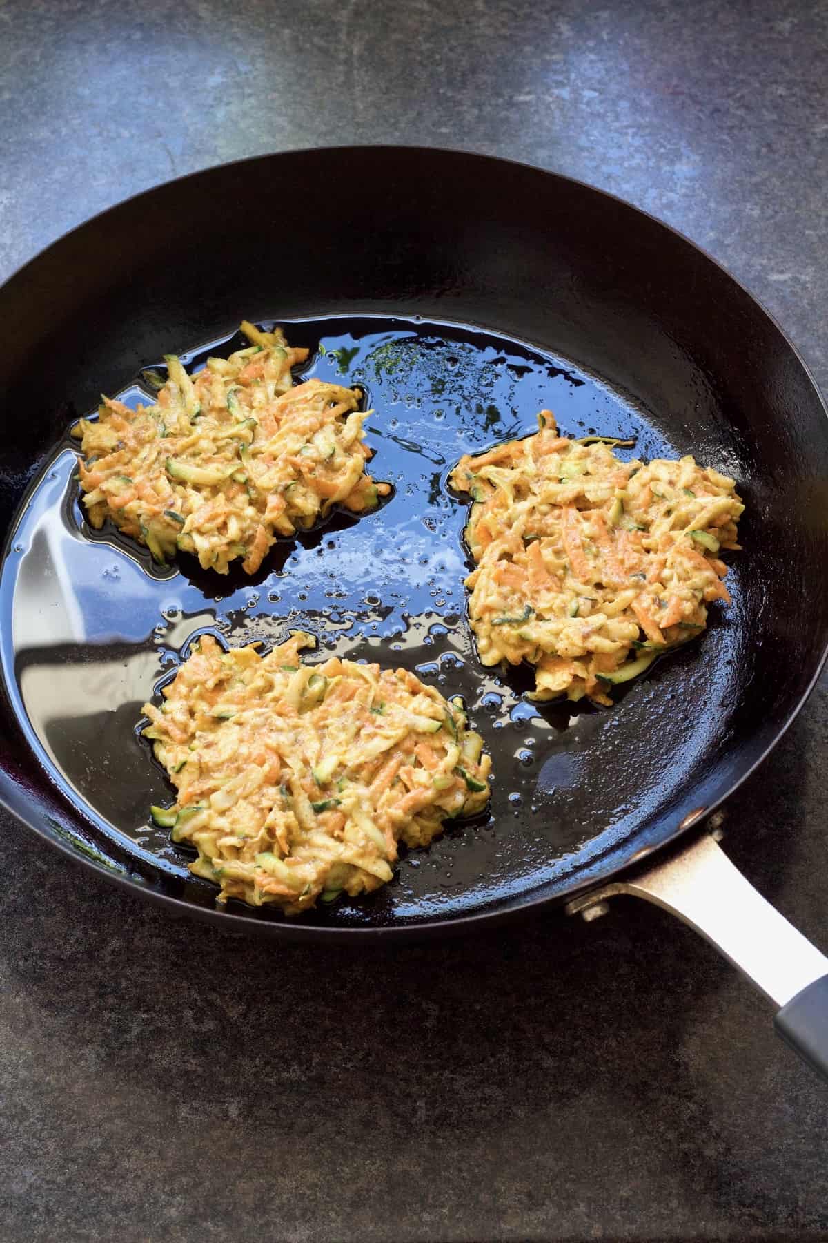 Three fritters in a frying pan.