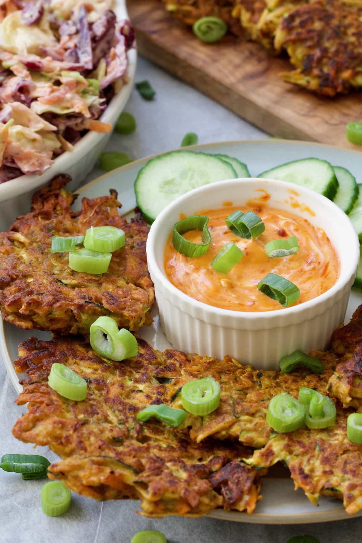 Vegan vegetable fritters on a plate with spring onions and bowl of sauce.