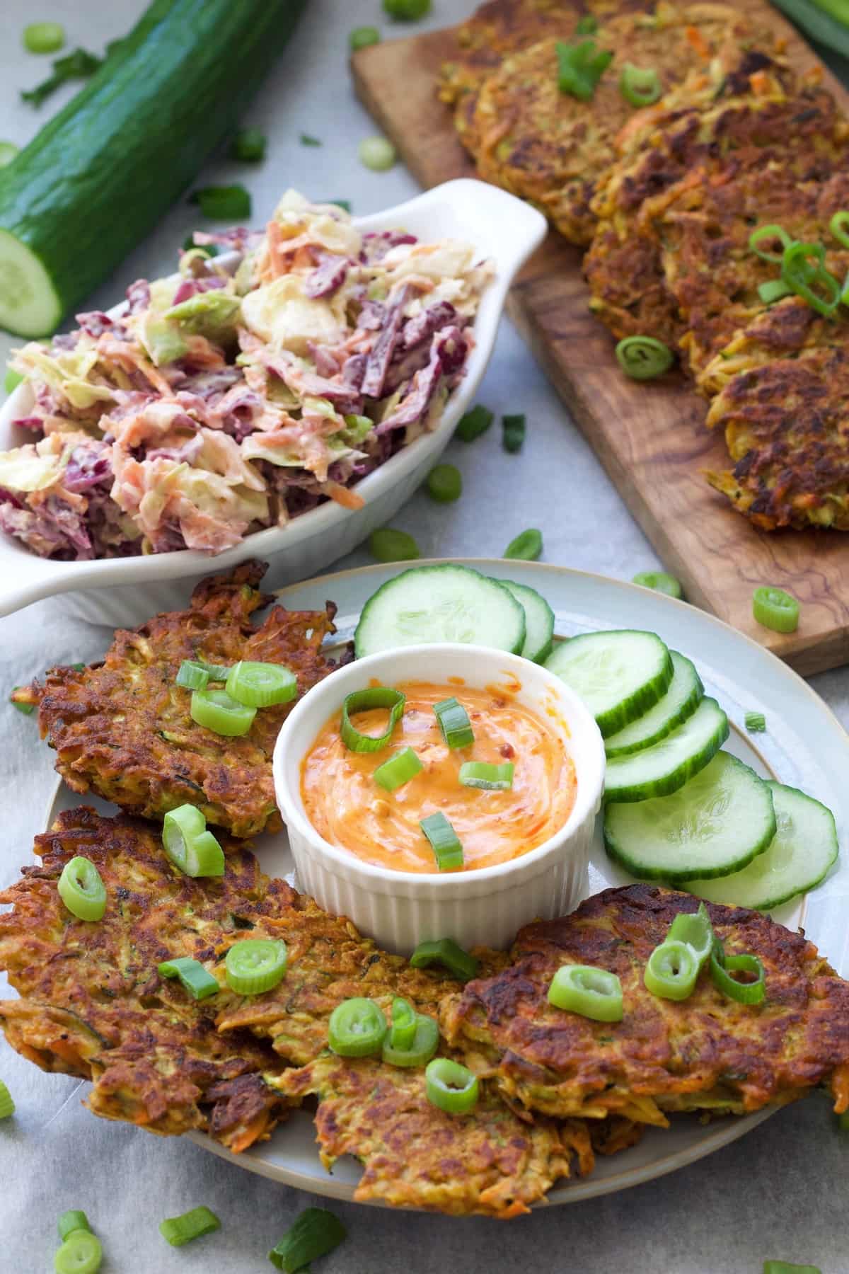 Vegan vegetable fritters on a plate with cucumber slices & sauce.