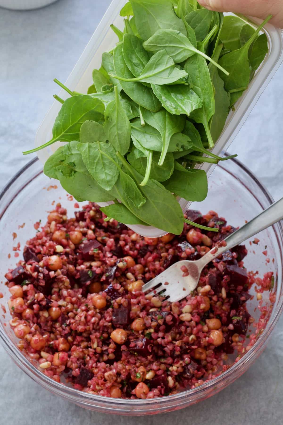 Spinach being added into the bowl with buckwheat salad.