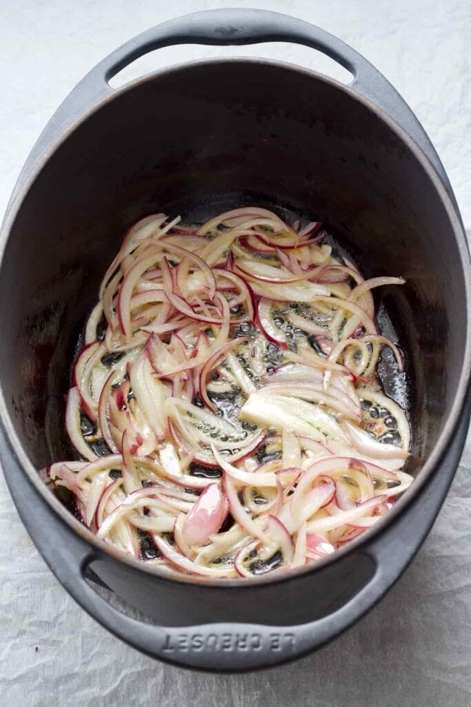 Sliced red onion frying in a pot.