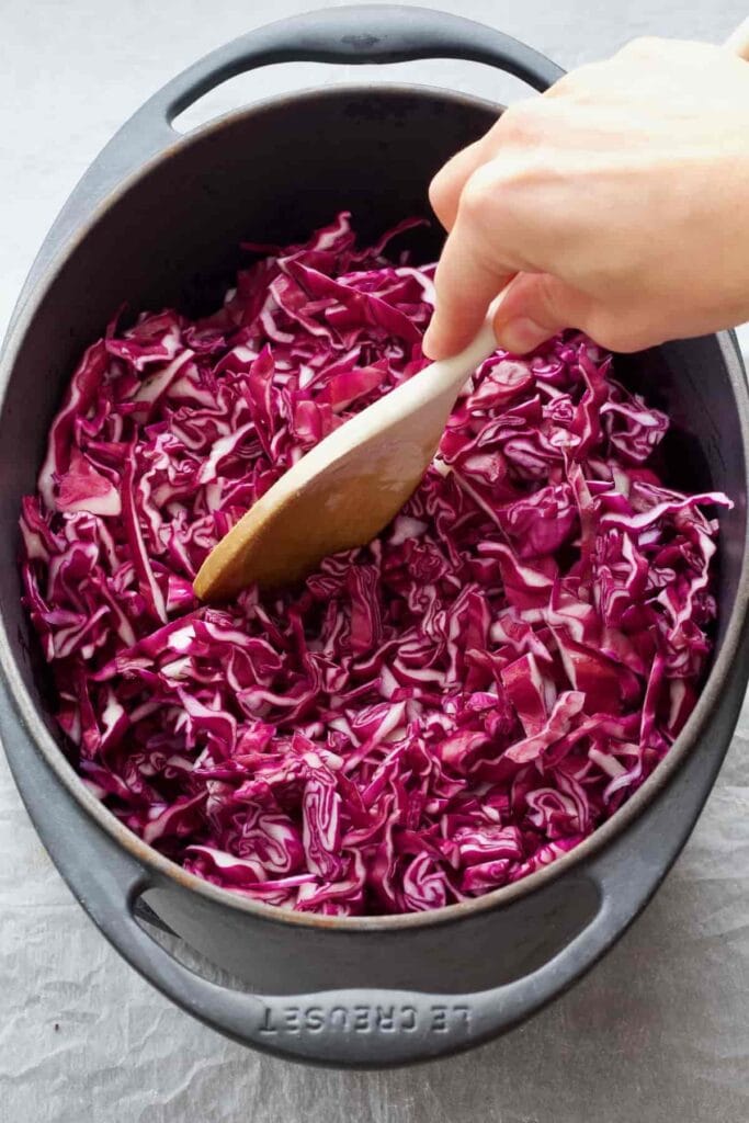 Hand stirring red cabbage with a wooden spoon.