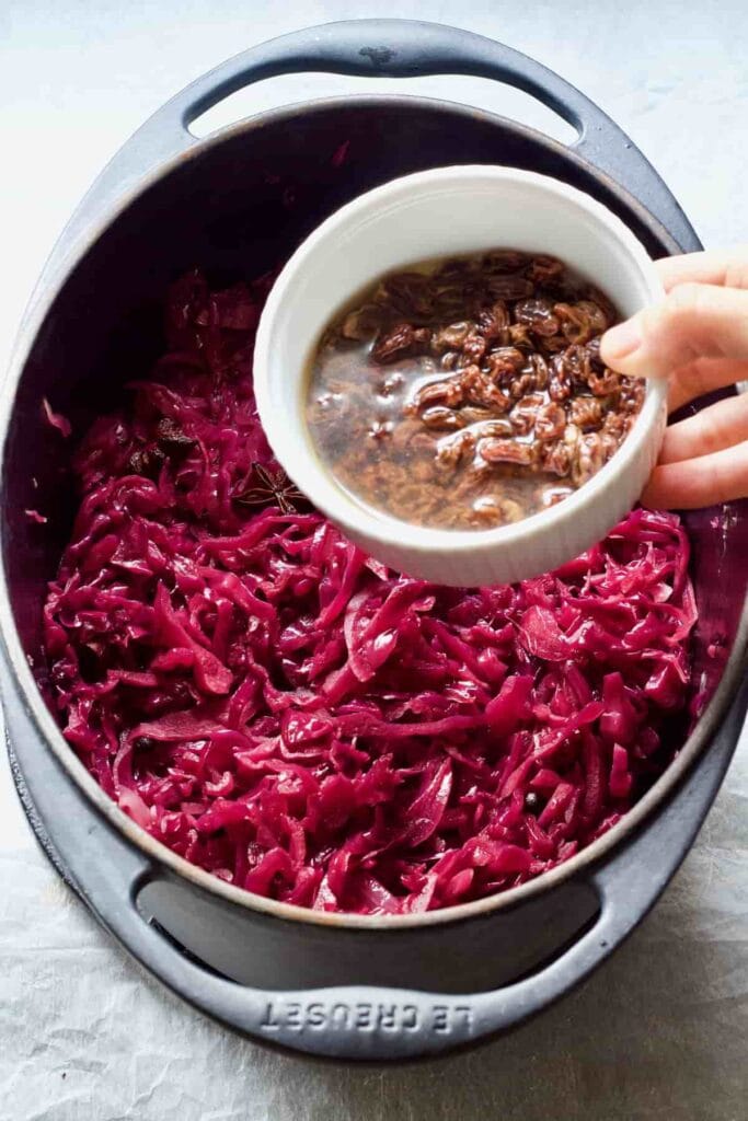 Raisins with liquid being added to the pot with cabbage.
