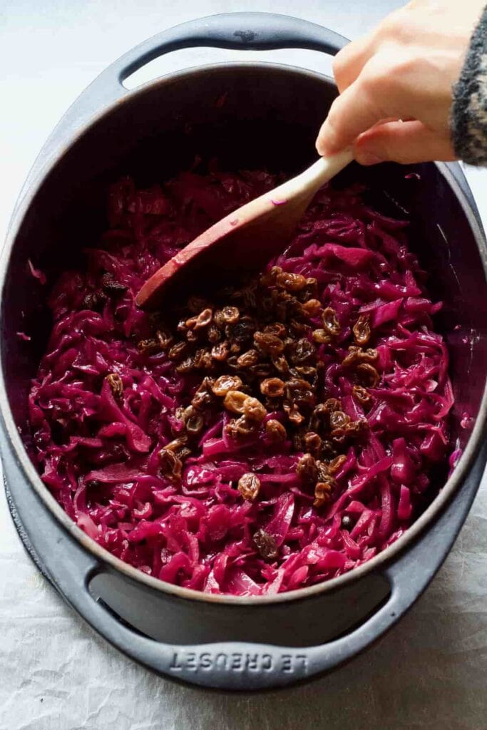 Pot with red cabbage and raisins on top being stirred.
