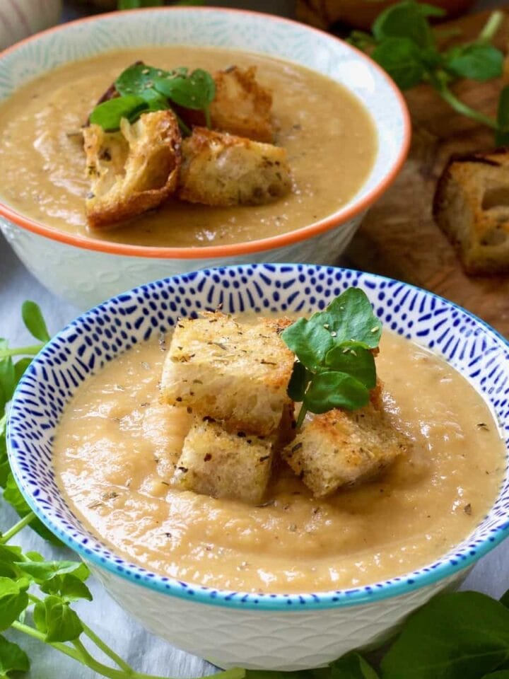 Square close up of two bowls with celeriac and sweet potato soup.