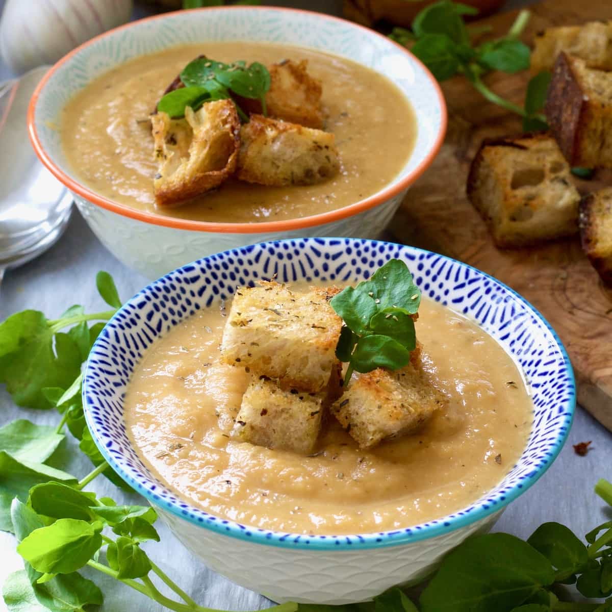 Square close up of two bowls with celeriac and sweet potato soup.