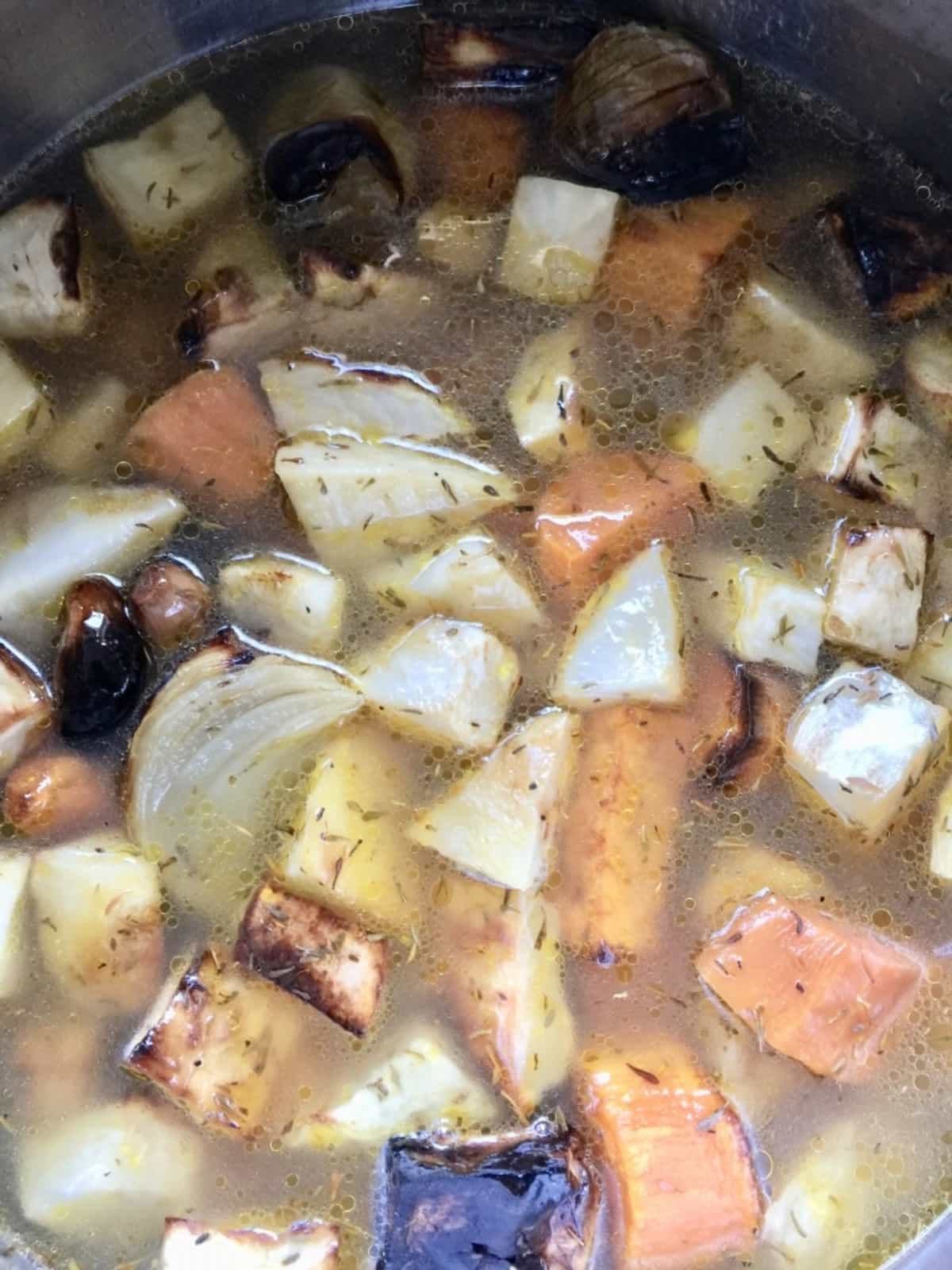 Roasted vegetable chunks in a pot with veggie stock.
