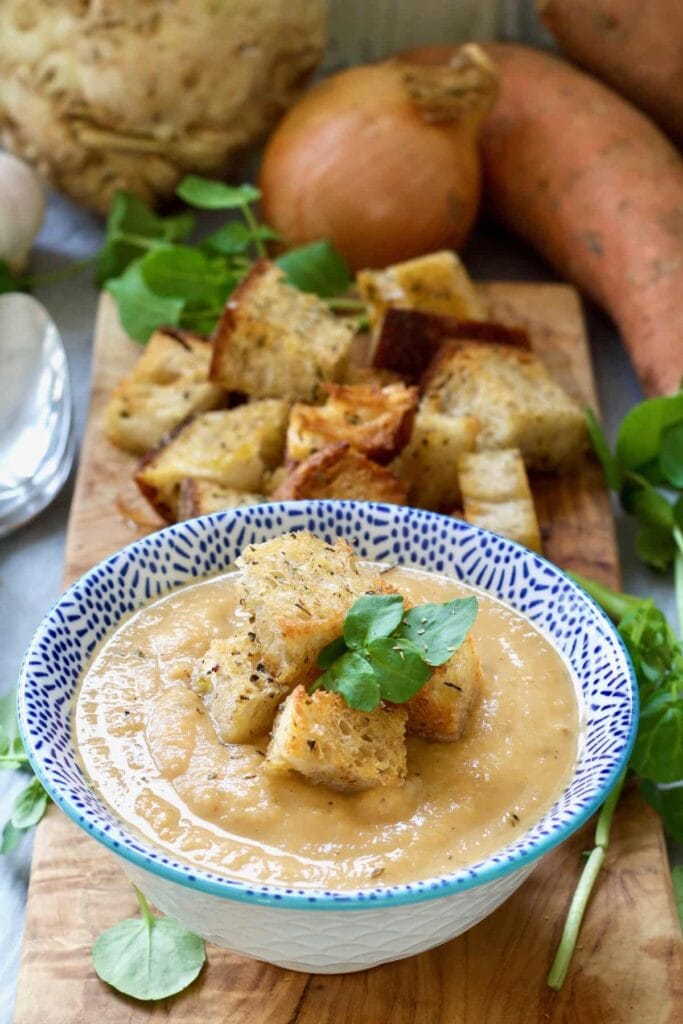 Bowl of celeriac & sweet potato soup on a board with croutons.