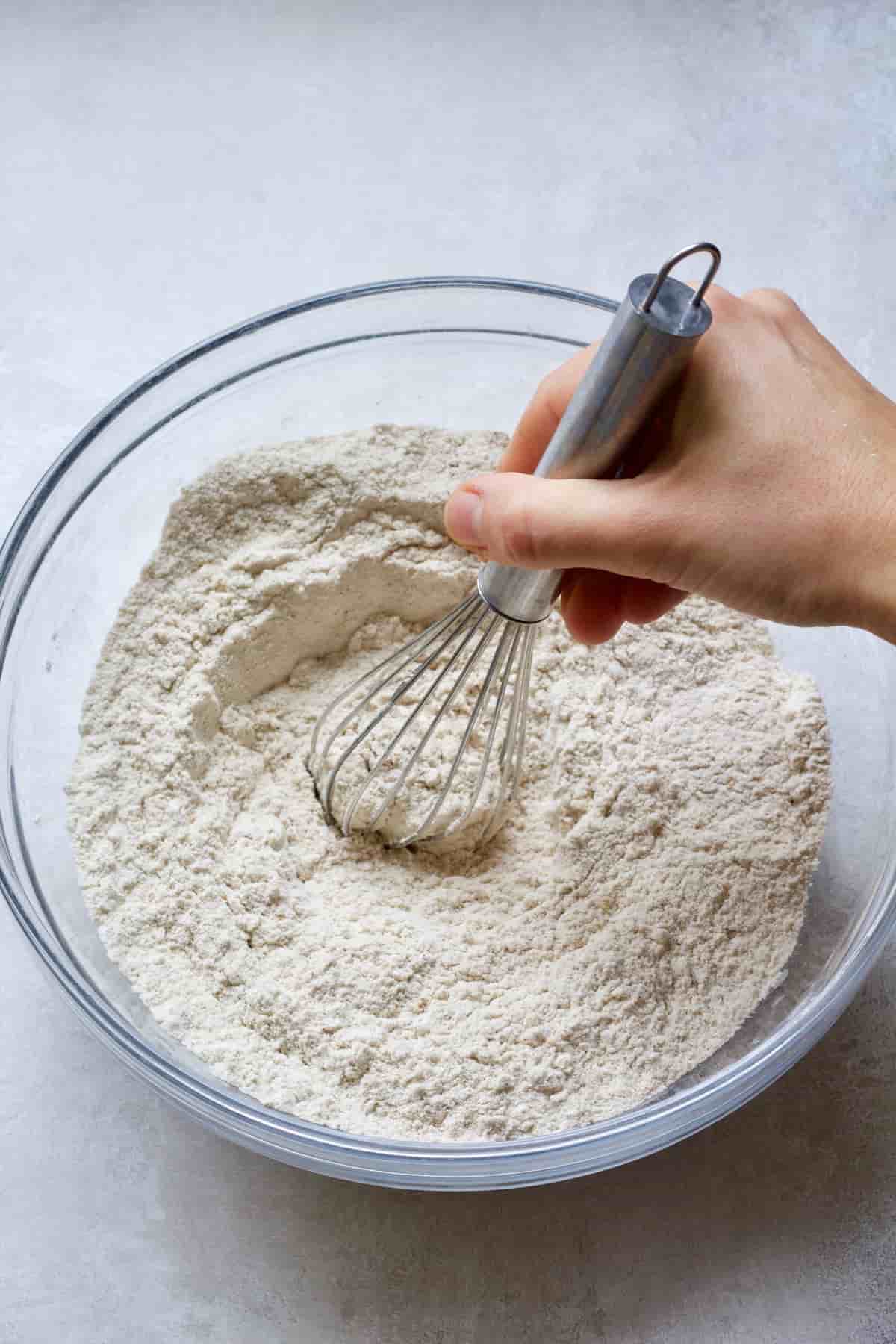 Hand mixing flour and spices in a bowl with a whisk.