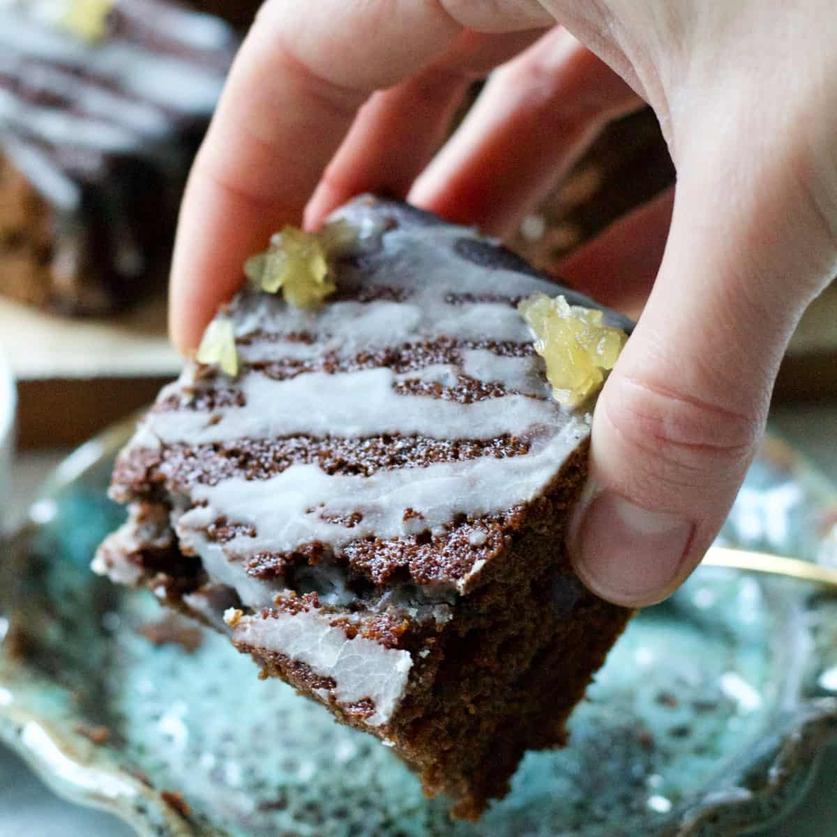 Hand holding gingerbread cake square showing icing.