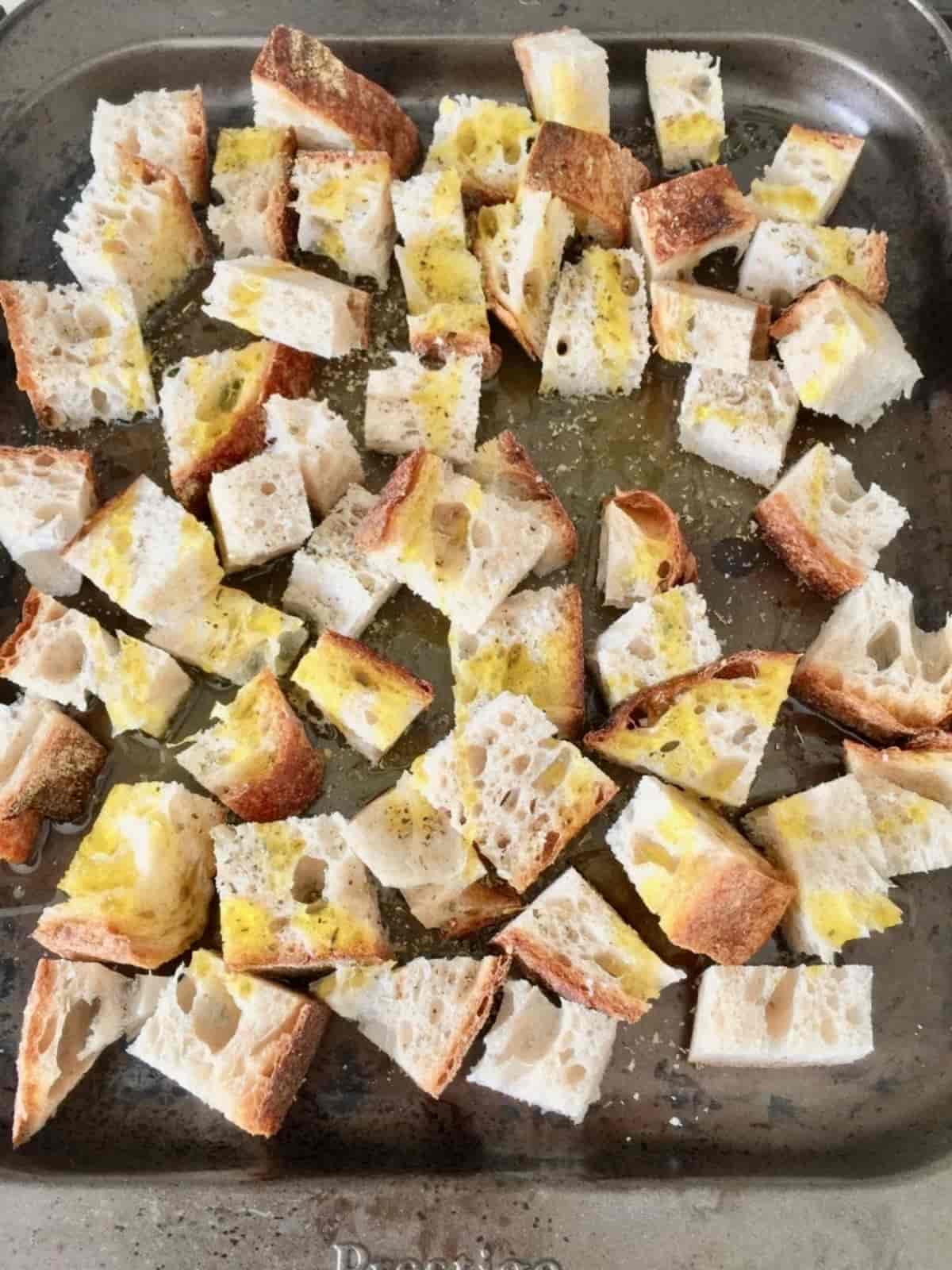 Chunks of bread sprinkled with oil & seasoning on a baking tray.